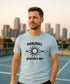 Man wearing a light blue t-shirt with pickleball design and text on an outdoor court with city skyline.